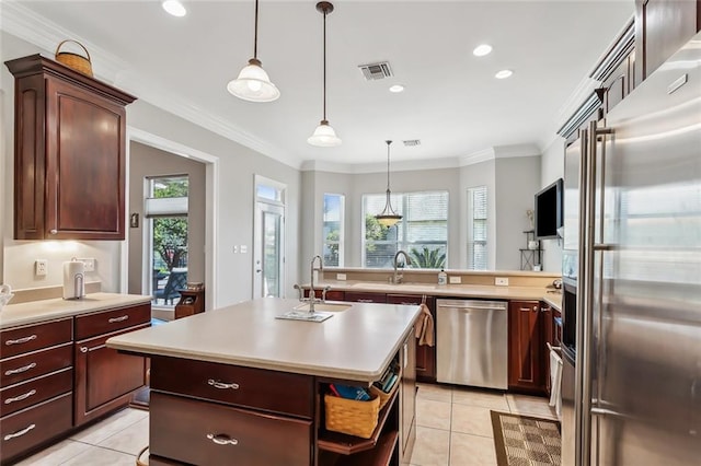 kitchen with an island with sink, stainless steel appliances, crown molding, decorative light fixtures, and light tile patterned floors