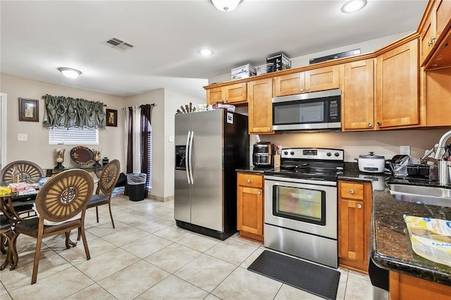 kitchen with light tile patterned flooring, stainless steel appliances, dark stone countertops, and sink