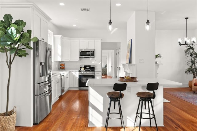 kitchen with decorative backsplash, white cabinets, light wood-type flooring, decorative light fixtures, and stainless steel appliances