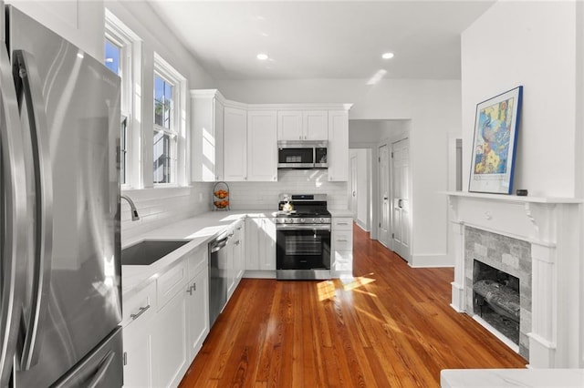 kitchen with sink, a tile fireplace, white cabinetry, stainless steel appliances, and hardwood / wood-style flooring