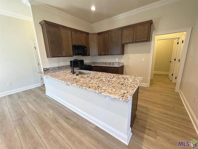 kitchen with a peninsula, light wood finished floors, light stone countertops, a sink, and black appliances