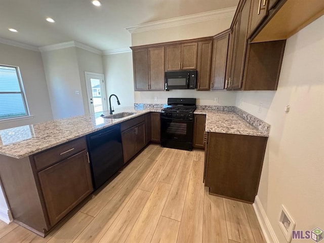 kitchen with a sink, a peninsula, light wood-style flooring, light stone countertops, and black appliances