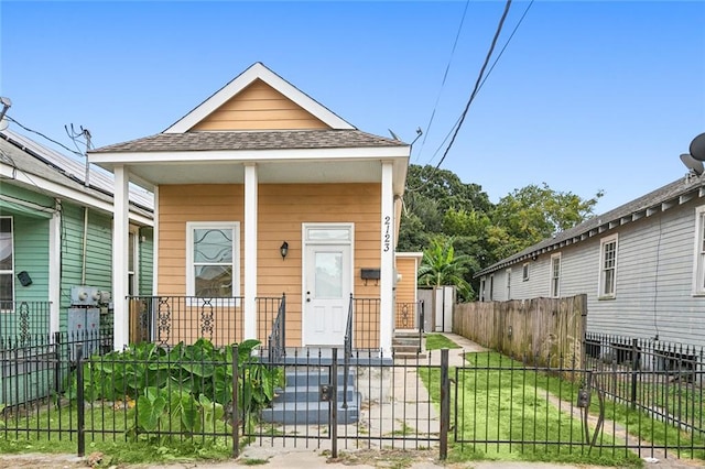 shotgun-style home with a fenced front yard, a porch, and a shingled roof