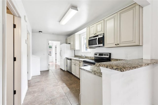 kitchen featuring light tile patterned floors, a peninsula, cream cabinets, stainless steel appliances, and a sink