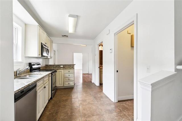 kitchen featuring visible vents, a peninsula, a sink, stainless steel appliances, and cream cabinetry