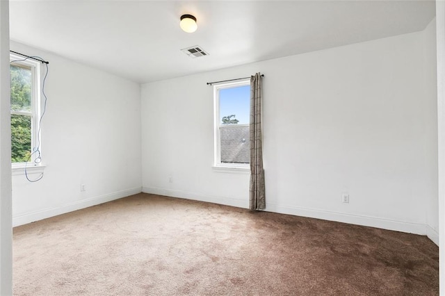 carpeted empty room featuring a wealth of natural light, visible vents, and baseboards