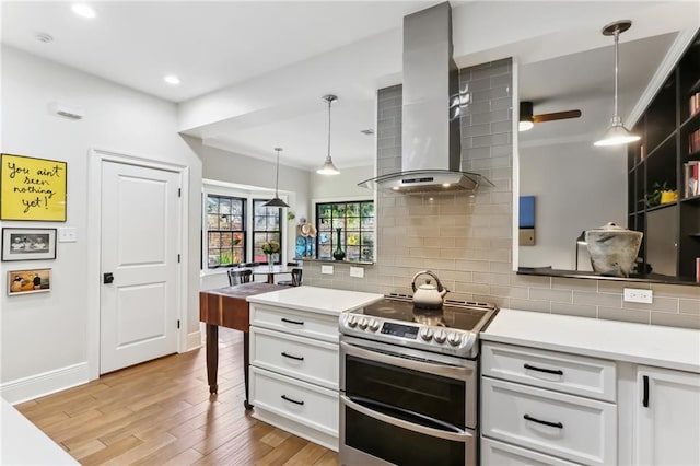 kitchen with electric range, wall chimney exhaust hood, hanging light fixtures, white cabinets, and light wood-type flooring