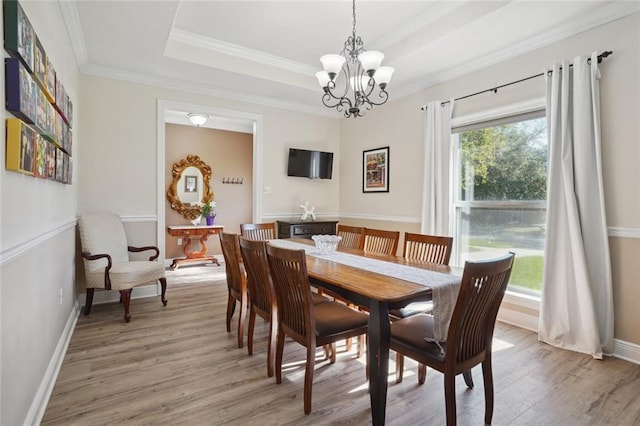 dining room featuring light wood-type flooring, an inviting chandelier, ornamental molding, and a tray ceiling