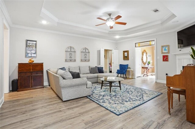 living room featuring ceiling fan, crown molding, light hardwood / wood-style flooring, and a raised ceiling