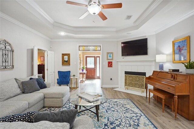 living room with ceiling fan, crown molding, a fireplace, and a raised ceiling