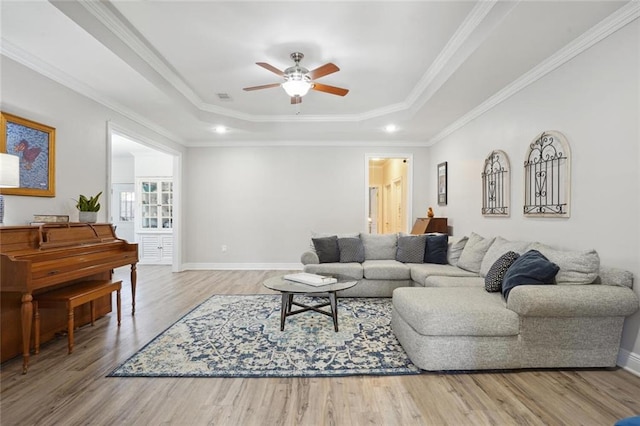 living room with ceiling fan, a tray ceiling, ornamental molding, and light hardwood / wood-style flooring