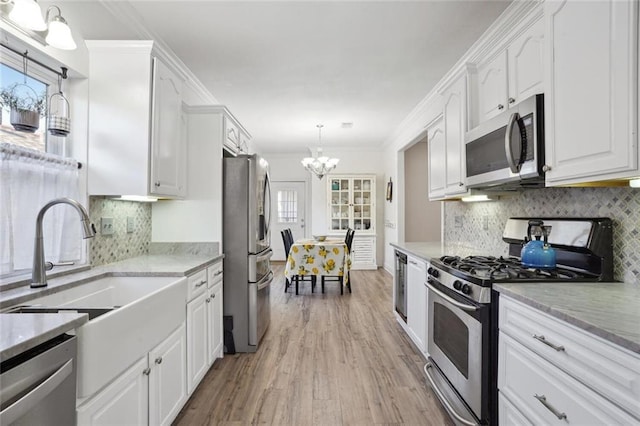 kitchen with appliances with stainless steel finishes, decorative light fixtures, white cabinetry, a notable chandelier, and crown molding