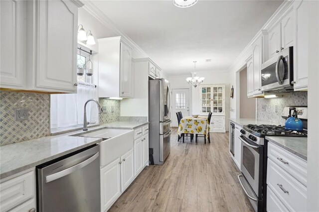 kitchen featuring pendant lighting, an inviting chandelier, crown molding, appliances with stainless steel finishes, and white cabinets