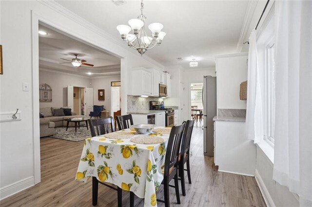 dining room featuring a tray ceiling, ceiling fan with notable chandelier, crown molding, and light hardwood / wood-style floors