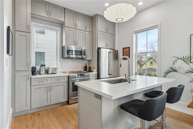 kitchen with backsplash, stainless steel appliances, sink, pendant lighting, and an island with sink