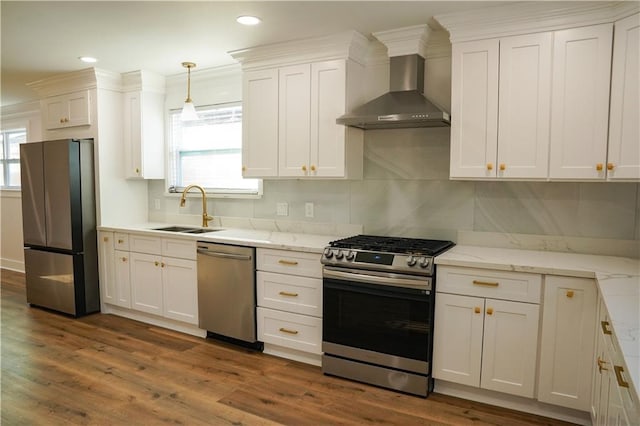 kitchen featuring wall chimney range hood, hanging light fixtures, stainless steel appliances, hardwood / wood-style floors, and sink