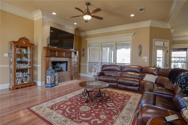 living room with light hardwood / wood-style floors, ornamental molding, and a tiled fireplace