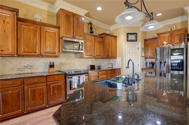 kitchen featuring appliances with stainless steel finishes, sink, light hardwood / wood-style floors, decorative light fixtures, and ornamental molding