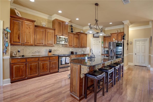 kitchen featuring stainless steel appliances, a center island with sink, a breakfast bar, pendant lighting, and light wood-type flooring