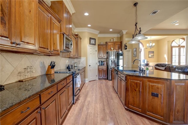 kitchen with sink, light hardwood / wood-style floors, stainless steel appliances, pendant lighting, and a kitchen island with sink