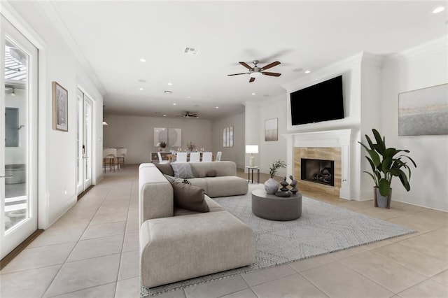 living room featuring a tiled fireplace, crown molding, light tile patterned flooring, and ceiling fan