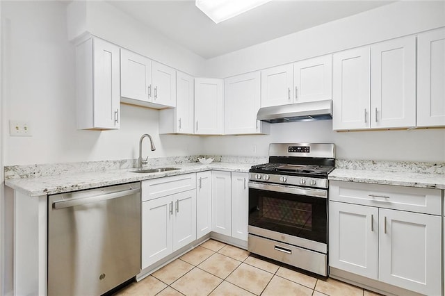 kitchen featuring appliances with stainless steel finishes, white cabinetry, sink, light tile patterned flooring, and light stone counters