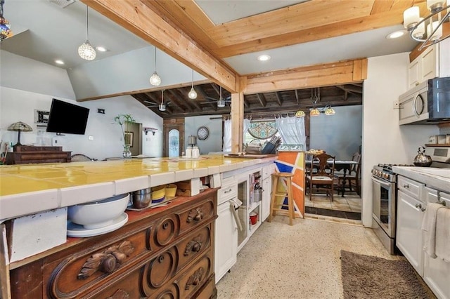 kitchen with appliances with stainless steel finishes, lofted ceiling with beams, white cabinetry, decorative light fixtures, and tile counters