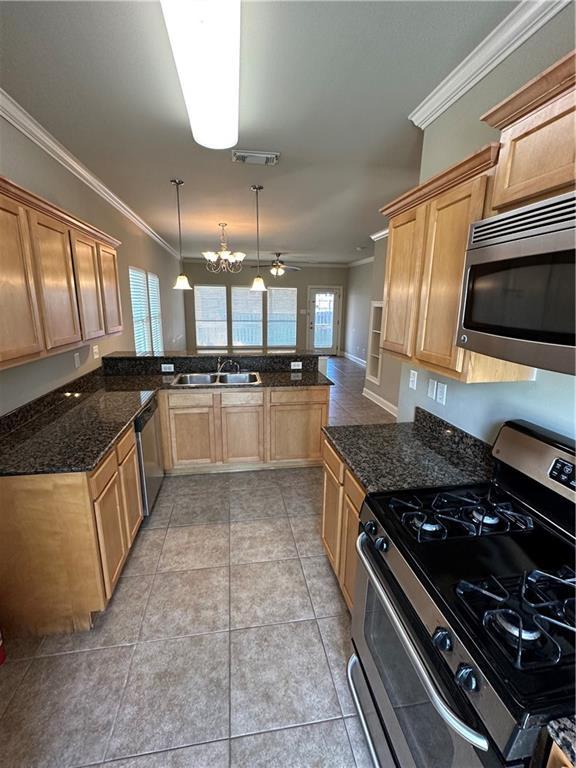 kitchen with crown molding, ceiling fan with notable chandelier, appliances with stainless steel finishes, a peninsula, and a sink