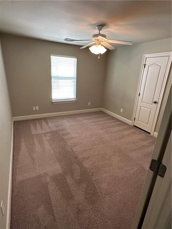 carpeted spare room with visible vents, baseboards, and ceiling fan