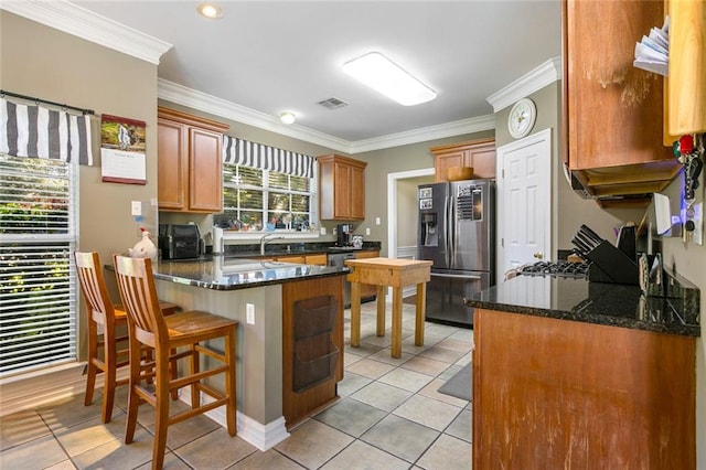 kitchen featuring light tile patterned flooring, kitchen peninsula, stainless steel appliances, dark stone countertops, and ornamental molding