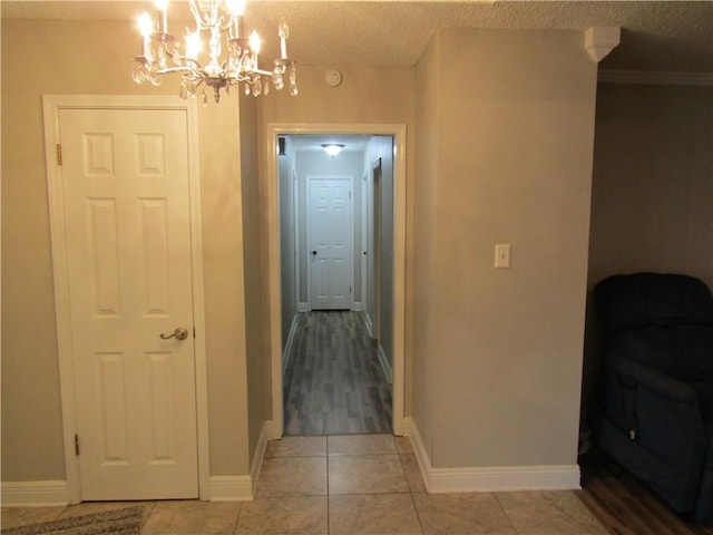 hallway featuring ornamental molding, a textured ceiling, a chandelier, and light tile patterned floors