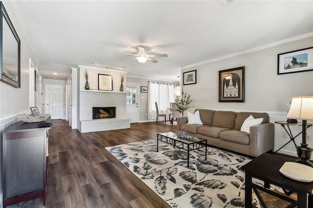 living room featuring crown molding, ceiling fan, dark wood-type flooring, and a brick fireplace