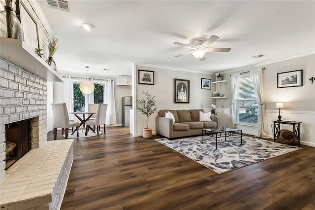 living room with ceiling fan, a brick fireplace, a healthy amount of sunlight, and dark hardwood / wood-style flooring