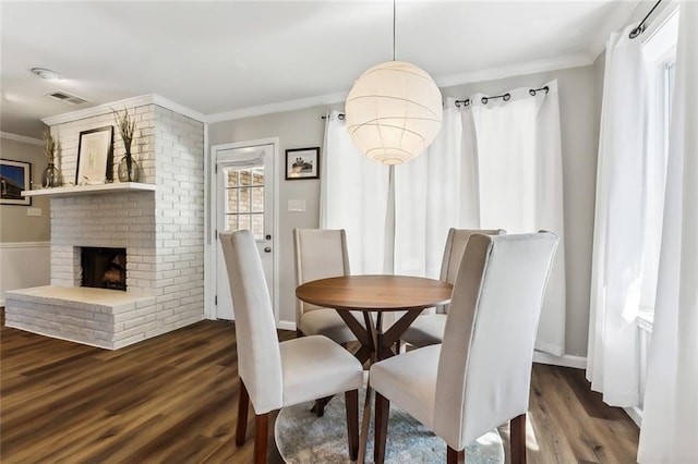 dining space with dark wood-type flooring, a brick fireplace, and crown molding