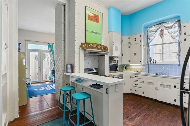 kitchen with kitchen peninsula, white cabinets, decorative backsplash, a breakfast bar area, and dark hardwood / wood-style floors