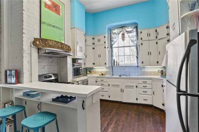 kitchen featuring appliances with stainless steel finishes, backsplash, kitchen peninsula, white cabinets, and dark hardwood / wood-style floors