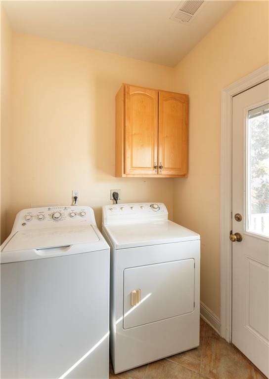 clothes washing area with washer and dryer, light tile patterned flooring, and cabinets