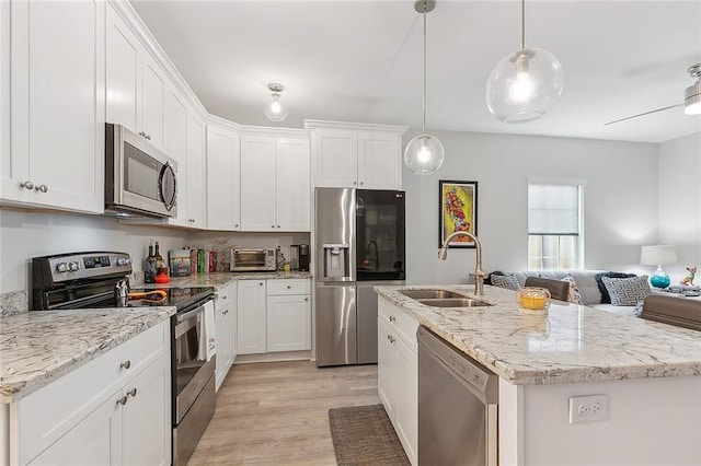 kitchen with an island with sink, stainless steel appliances, sink, pendant lighting, and white cabinetry