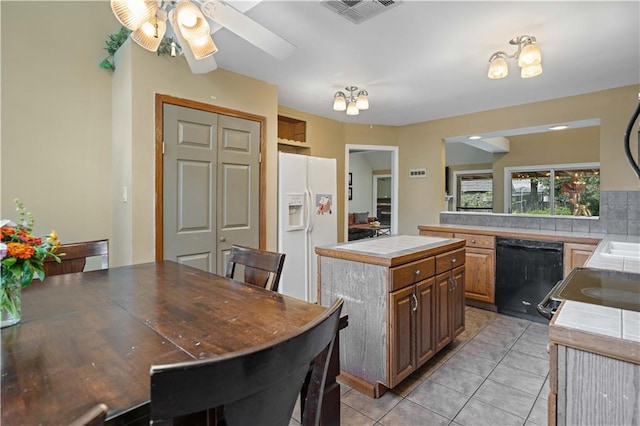 kitchen featuring black dishwasher, white fridge with ice dispenser, a kitchen island, tile counters, and light tile patterned floors