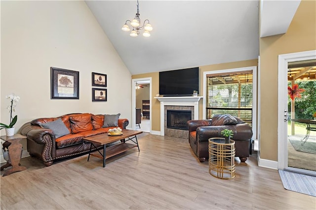 living room featuring a tiled fireplace, light hardwood / wood-style floors, high vaulted ceiling, and an inviting chandelier