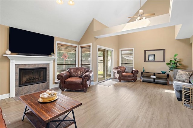 living room with light hardwood / wood-style floors, a tiled fireplace, high vaulted ceiling, and ceiling fan