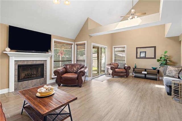 living room featuring light wood finished floors, a ceiling fan, baseboards, a tiled fireplace, and high vaulted ceiling