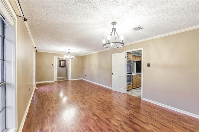 spare room with a textured ceiling, crown molding, a notable chandelier, and wood-type flooring