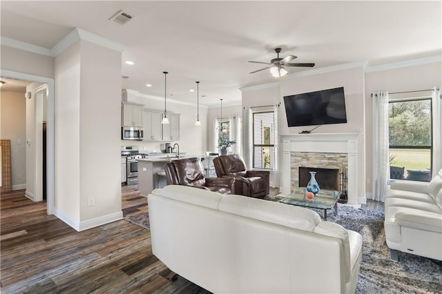 living room featuring ceiling fan, a healthy amount of sunlight, dark hardwood / wood-style floors, and a stone fireplace