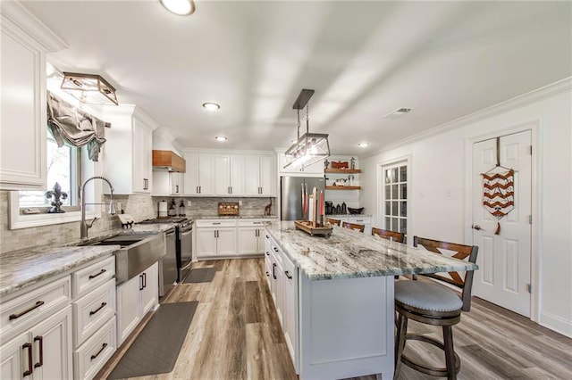 kitchen featuring stainless steel appliances, light stone countertops, a center island, light wood-type flooring, and white cabinetry