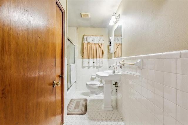 bathroom with toilet, a shower with shower door, tile patterned floors, and tile walls