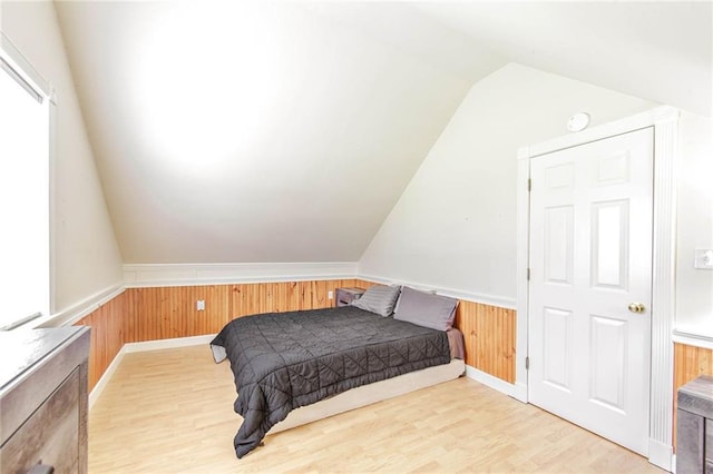 bedroom featuring wood walls, vaulted ceiling, and wainscoting