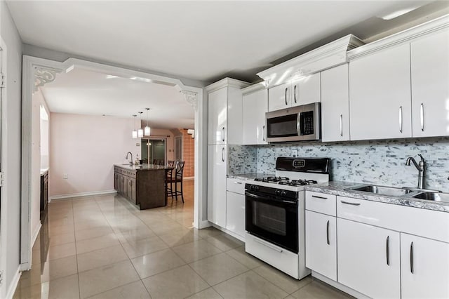 kitchen with decorative backsplash, white cabinets, light tile patterned floors, gas range gas stove, and sink