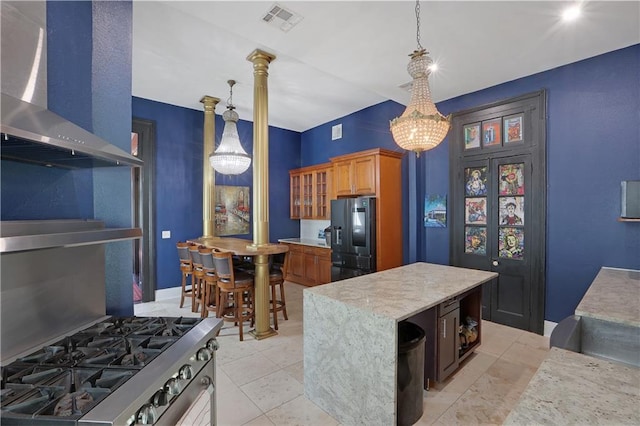 kitchen with a kitchen island, ornate columns, wall chimney exhaust hood, pendant lighting, and appliances with stainless steel finishes