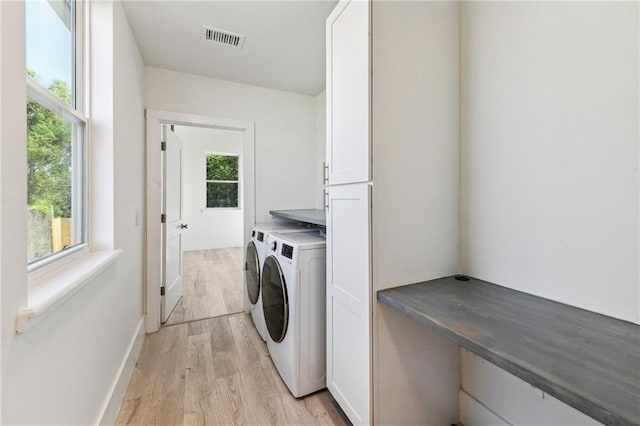 clothes washing area featuring a healthy amount of sunlight, cabinets, light wood-type flooring, and washing machine and clothes dryer